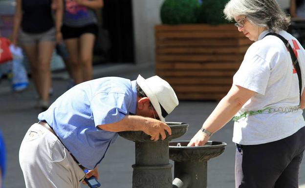 Dos personas se refrescan en una fuente de la avenida del Acueducto.