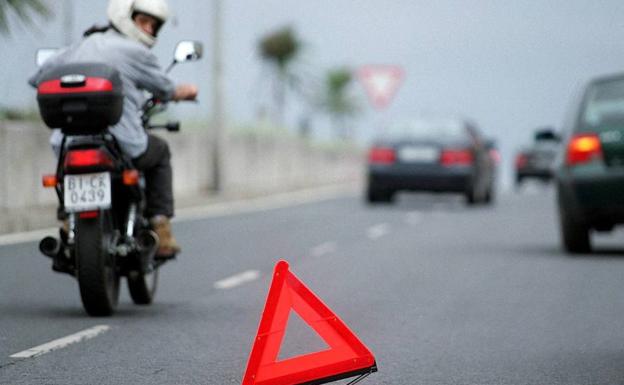 Un motorista observa un triángulo que avisa de la avería de un coche./Luis Ángel Gómez/El Correo