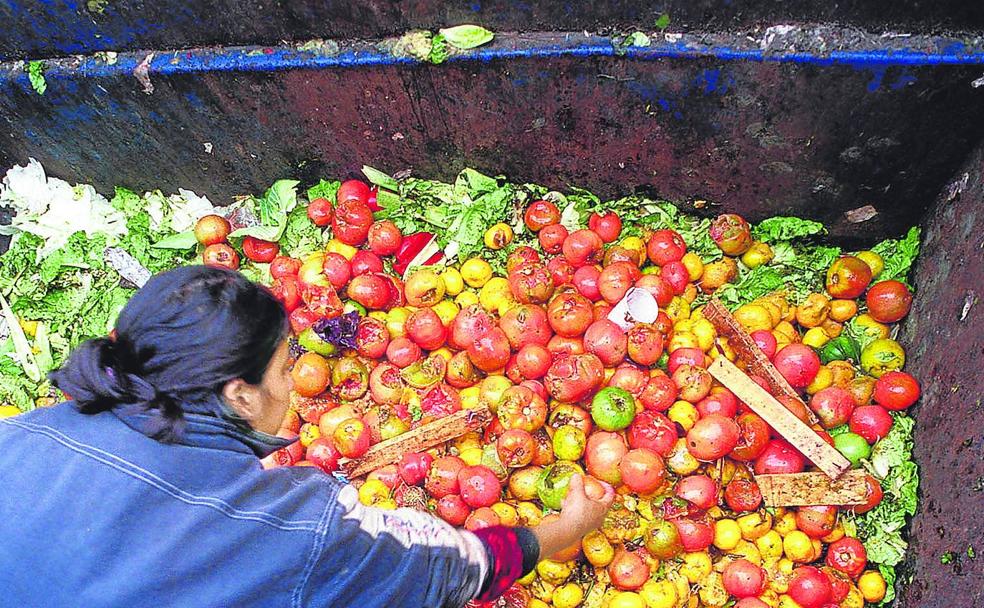 Una mujer recoge alimentos arrojados a un contenedor a las puertas de una gran superficie comercial./AFP